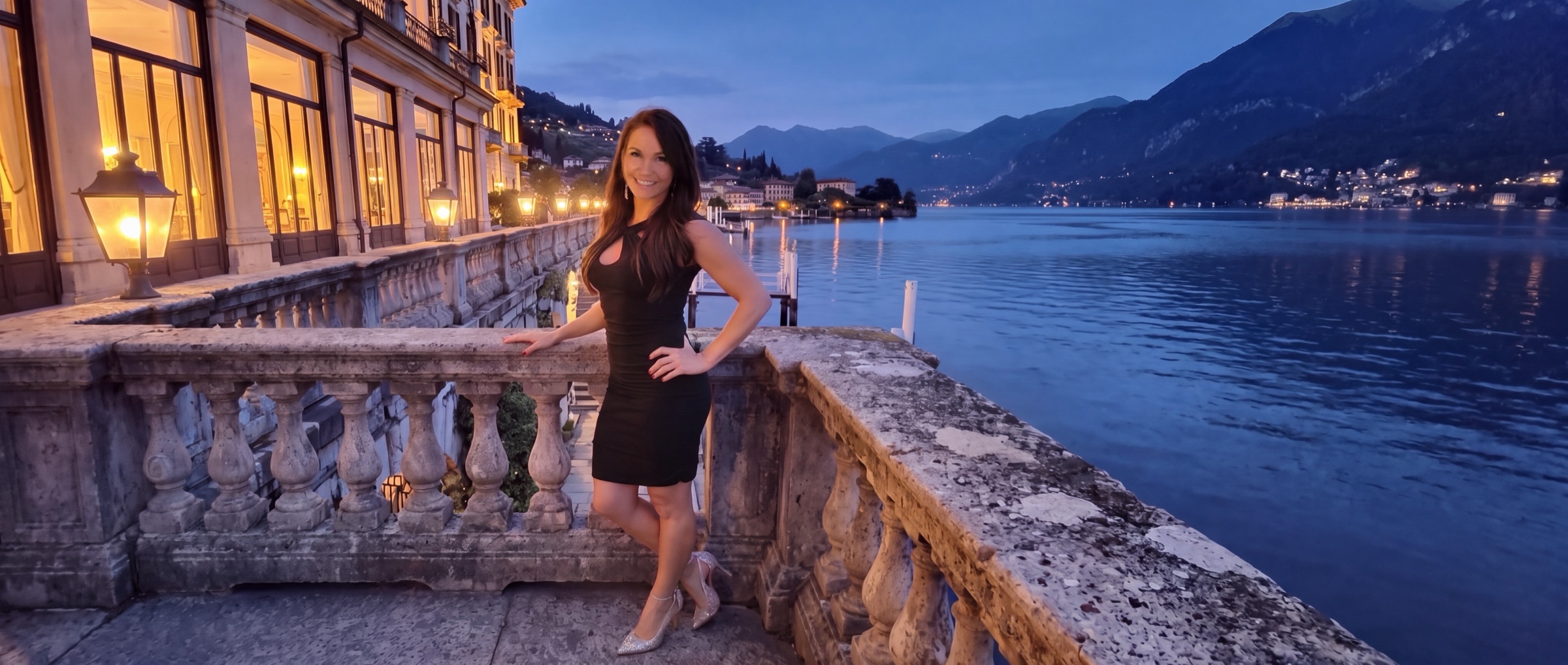 Sheri in a black dress on a hotel terrace above a lake at dusk